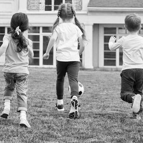 Three children play soccer in the backyard of a house.
